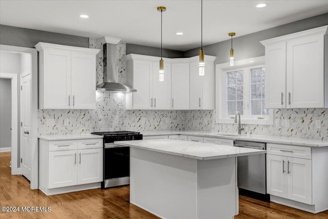 kitchen with stainless steel appliances, white cabinetry, a kitchen island, and wall chimney range hood