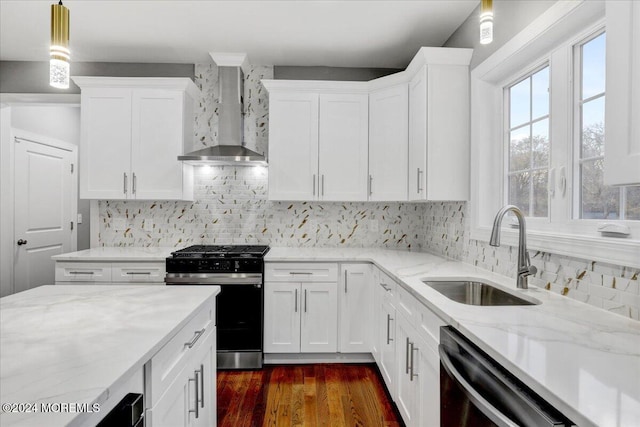 kitchen with stainless steel appliances, wall chimney range hood, sink, pendant lighting, and white cabinetry