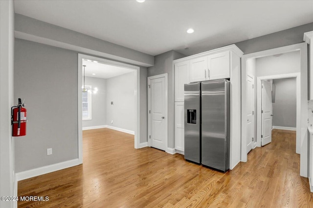 kitchen with white cabinets, stainless steel fridge, an inviting chandelier, and light hardwood / wood-style flooring