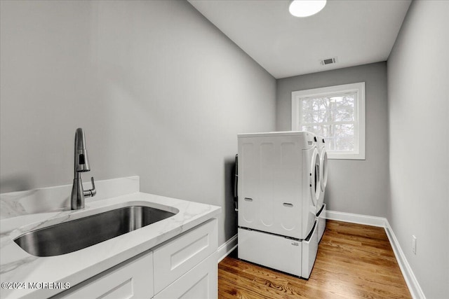 laundry room with washing machine and dryer, cabinets, sink, and light hardwood / wood-style floors