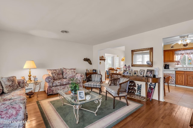 living room featuring ceiling fan, light hardwood / wood-style floors, sink, and baseboard heating