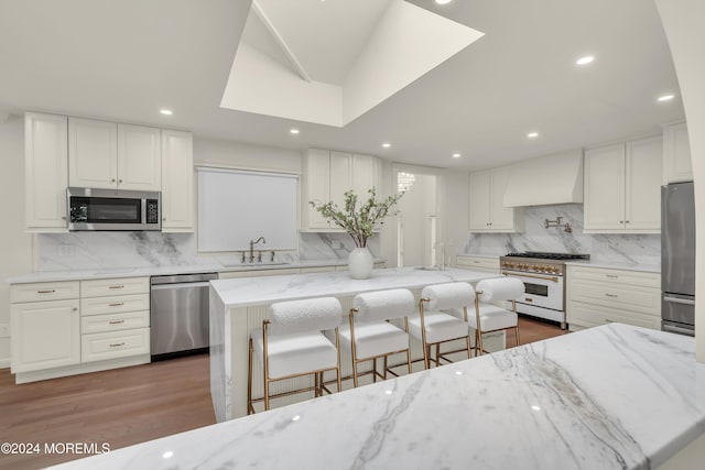 kitchen featuring premium range hood, white cabinets, a large island, light stone counters, and stainless steel appliances