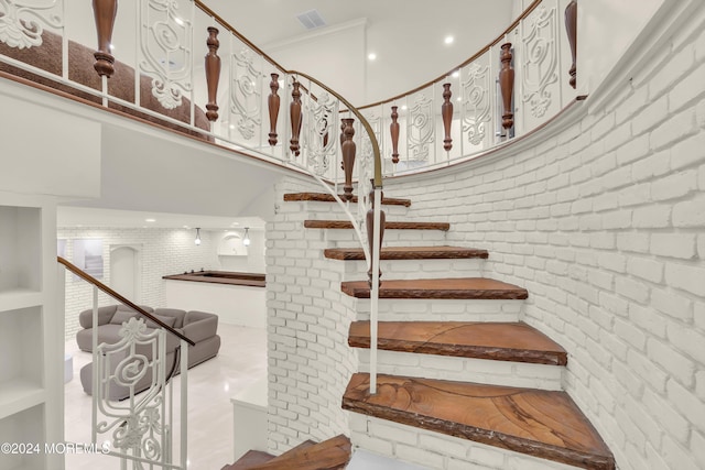 staircase with crown molding and brick wall