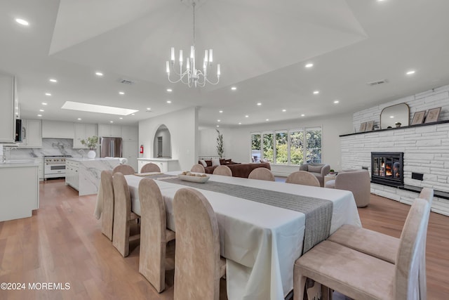 dining room with light hardwood / wood-style floors, a stone fireplace, and a notable chandelier