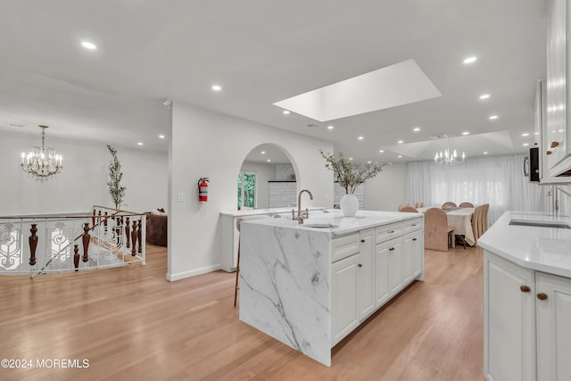 kitchen featuring a skylight, sink, a kitchen island with sink, white cabinets, and light wood-type flooring