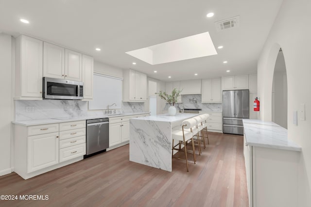 kitchen with light stone countertops, appliances with stainless steel finishes, a skylight, and white cabinetry