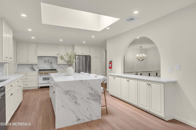 kitchen featuring light stone countertops, stainless steel appliances, light hardwood / wood-style flooring, white cabinetry, and hanging light fixtures