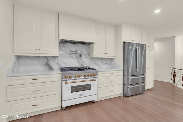 kitchen with decorative backsplash, custom range hood, premium appliances, and light hardwood / wood-style floors