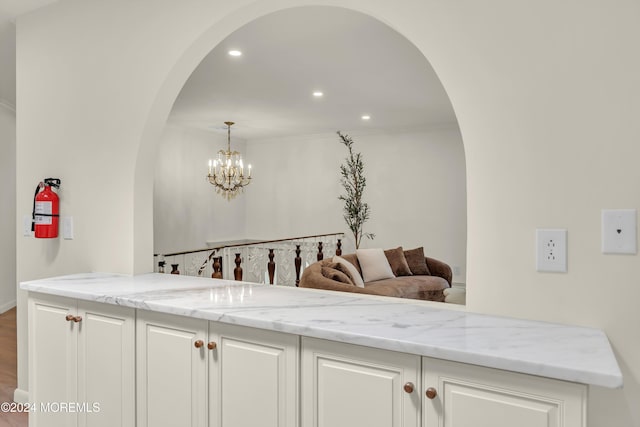 bar with hardwood / wood-style floors, an inviting chandelier, light stone countertops, ornamental molding, and white cabinetry