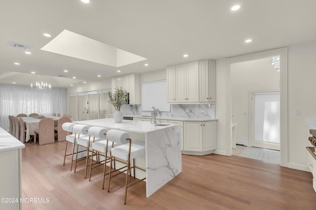 kitchen with backsplash, light hardwood / wood-style flooring, light stone countertops, a large island, and white cabinetry