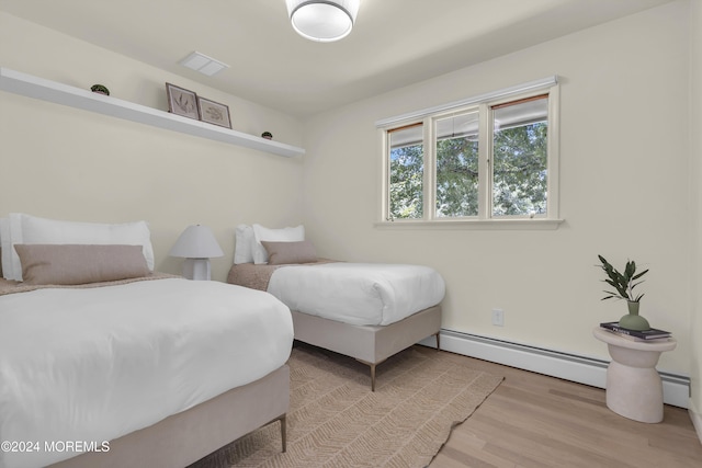 bedroom with light hardwood / wood-style flooring and a baseboard heating unit