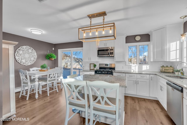 kitchen with sink, white cabinets, light stone counters, hanging light fixtures, and appliances with stainless steel finishes