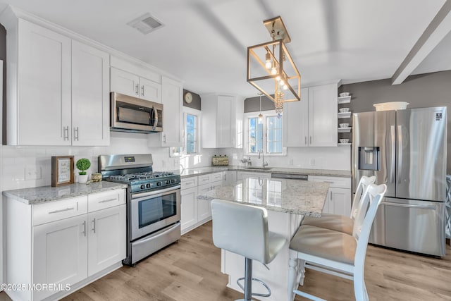 kitchen with appliances with stainless steel finishes, white cabinets, decorative light fixtures, and light stone countertops