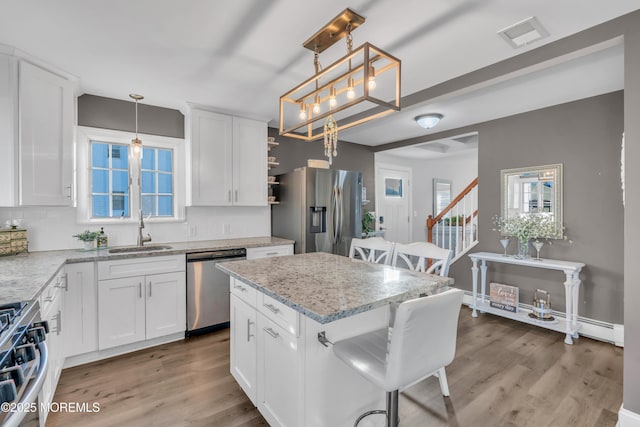 kitchen featuring sink, stainless steel appliances, white cabinetry, and hanging light fixtures