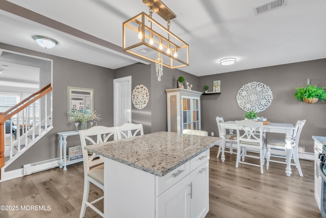 kitchen featuring light stone countertops, pendant lighting, a kitchen island, hardwood / wood-style flooring, and white cabinetry