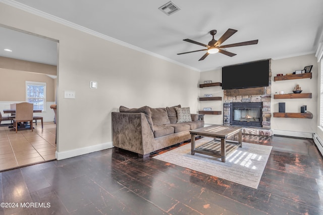 living room featuring dark hardwood / wood-style flooring, a stone fireplace, ceiling fan, and crown molding