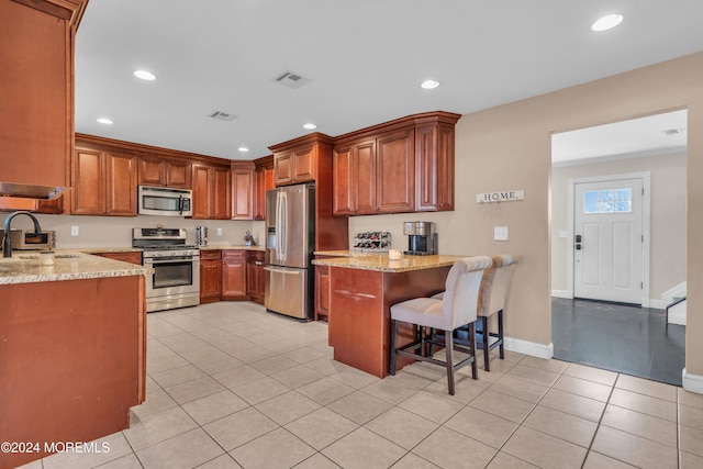 kitchen featuring a kitchen bar, sink, light stone counters, kitchen peninsula, and stainless steel appliances