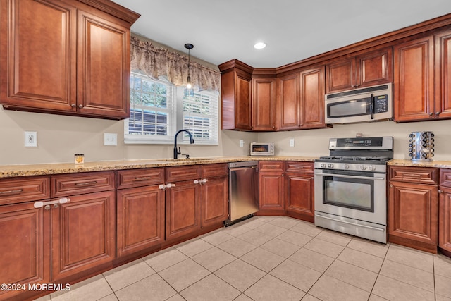 kitchen with light stone countertops, stainless steel appliances, sink, light tile patterned floors, and hanging light fixtures