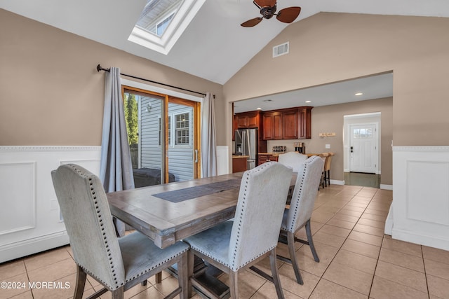 dining space with light tile patterned floors, ceiling fan, and vaulted ceiling with skylight