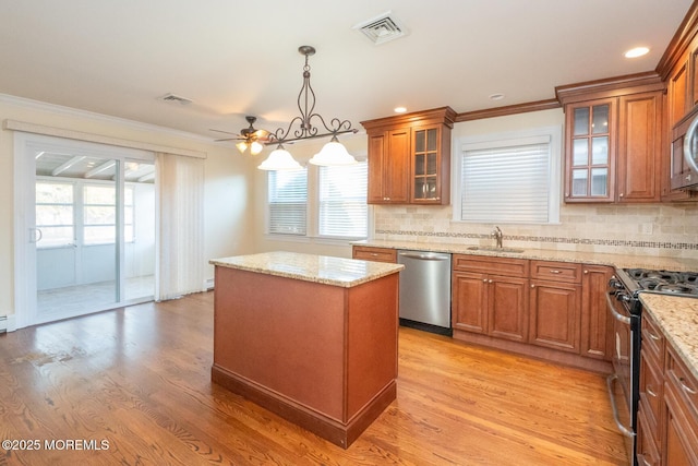 kitchen with sink, a kitchen island, pendant lighting, stainless steel appliances, and light hardwood / wood-style floors