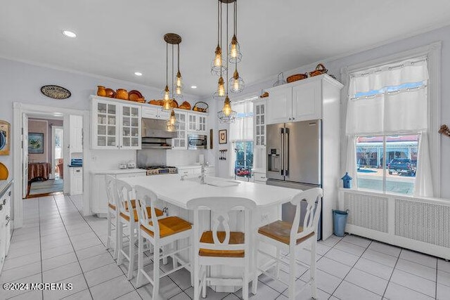 kitchen with white cabinets, an island with sink, light tile patterned flooring, and decorative light fixtures