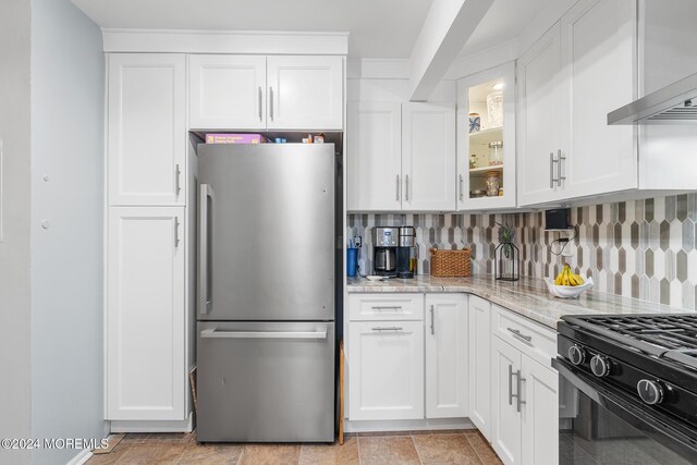 kitchen featuring stainless steel refrigerator, white cabinetry, light stone countertops, wall chimney range hood, and tasteful backsplash