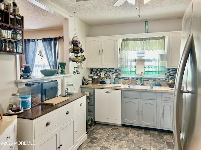 kitchen featuring a textured ceiling, sink, dishwasher, white cabinetry, and stainless steel refrigerator