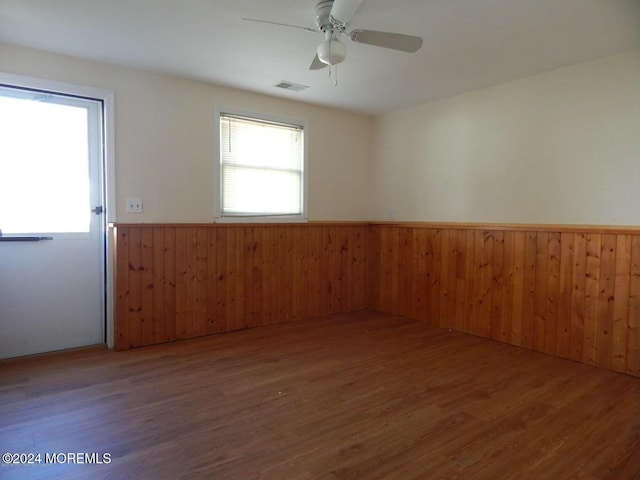 empty room featuring wooden walls, ceiling fan, and dark wood-type flooring