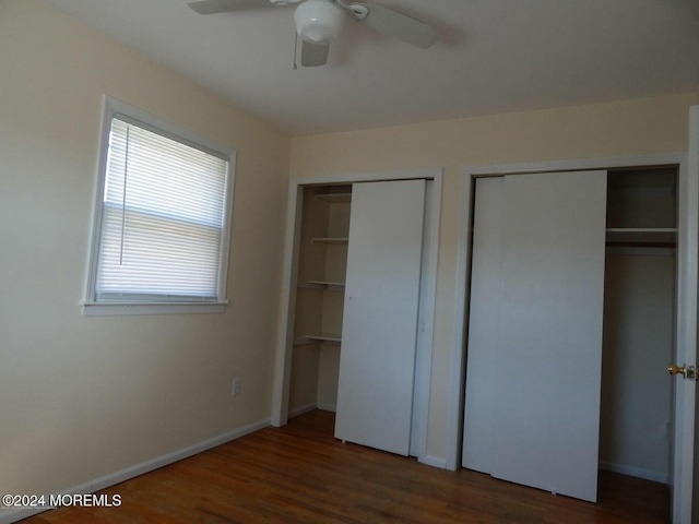 unfurnished bedroom with ceiling fan, dark hardwood / wood-style flooring, and two closets