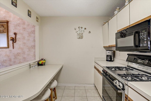 kitchen featuring gas range, a textured ceiling, white cabinetry, and light tile patterned flooring