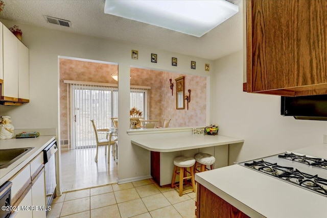 kitchen featuring white cabinets, stainless steel dishwasher, light tile patterned floors, a textured ceiling, and cooktop