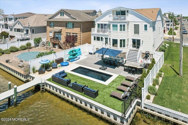 rear view of property featuring a lawn, a balcony, a water view, and a patio