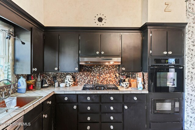 kitchen featuring decorative backsplash, sink, tile countertops, black oven, and stainless steel gas stovetop