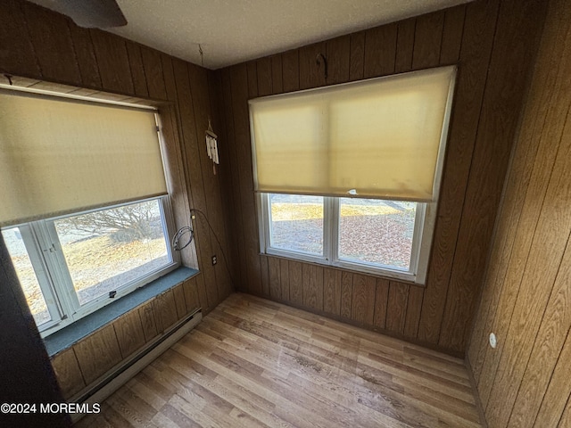 spare room featuring wood walls, a healthy amount of sunlight, a baseboard heating unit, and light hardwood / wood-style flooring