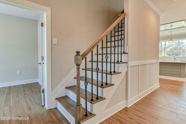 staircase featuring hardwood / wood-style floors, ornamental molding, and sink