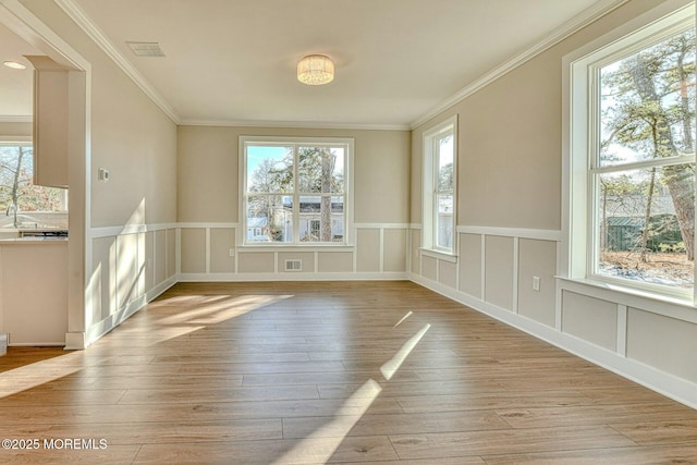 empty room with light hardwood / wood-style floors, plenty of natural light, and ornamental molding