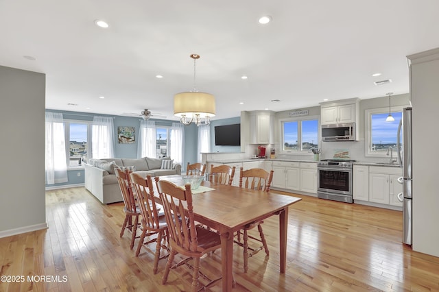 dining room with sink, light hardwood / wood-style floors, and ceiling fan with notable chandelier