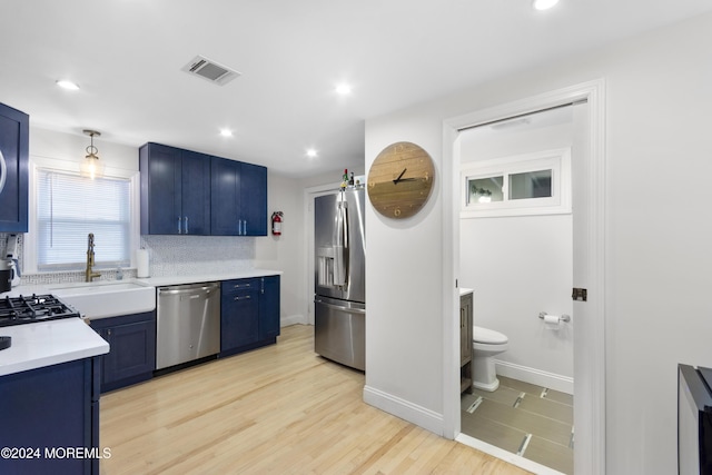 kitchen featuring appliances with stainless steel finishes, light wood-type flooring, blue cabinets, and backsplash