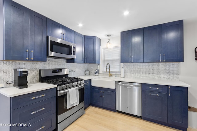 kitchen featuring decorative backsplash, appliances with stainless steel finishes, blue cabinets, sink, and light hardwood / wood-style floors