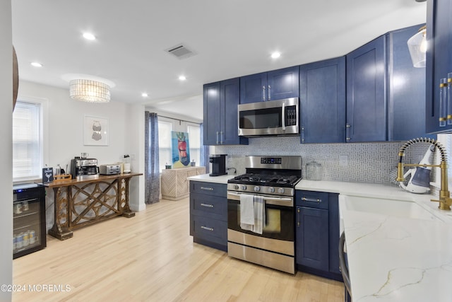 kitchen featuring blue cabinetry, sink, light stone counters, appliances with stainless steel finishes, and light wood-type flooring