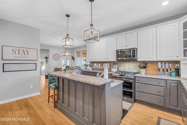 kitchen with pendant lighting, a kitchen breakfast bar, light stone countertops, appliances with stainless steel finishes, and white cabinetry