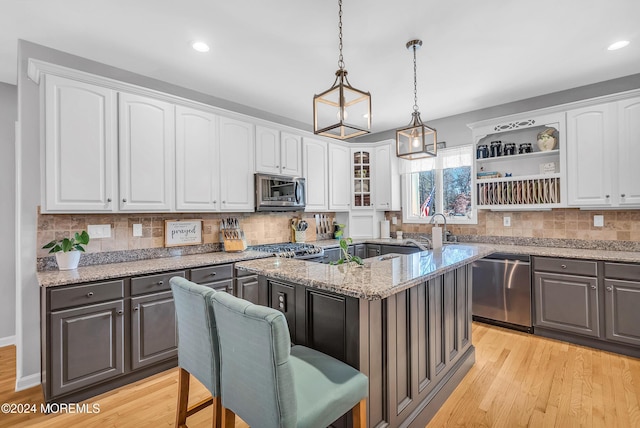 kitchen with white cabinetry, a center island, light stone counters, decorative light fixtures, and appliances with stainless steel finishes