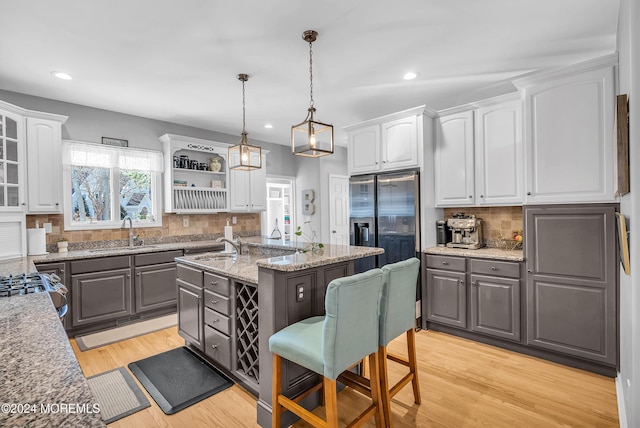 kitchen with a kitchen island with sink, sink, hanging light fixtures, decorative backsplash, and white cabinetry