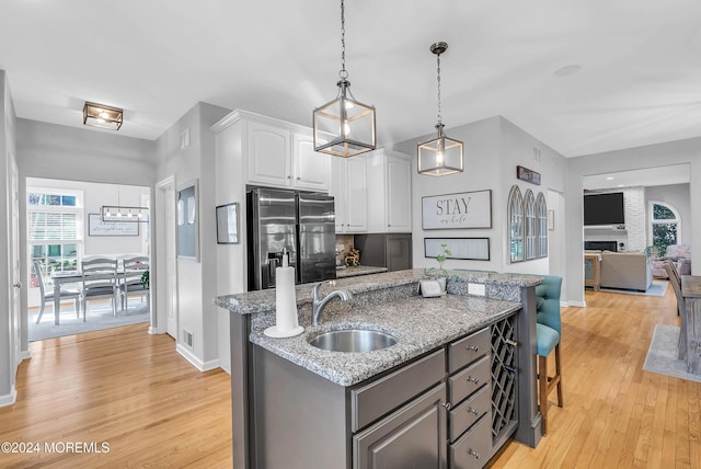 kitchen with sink, stainless steel fridge with ice dispenser, an island with sink, decorative light fixtures, and white cabinetry