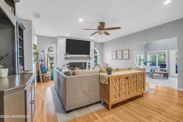 living room with a brick fireplace, ceiling fan, and light wood-type flooring