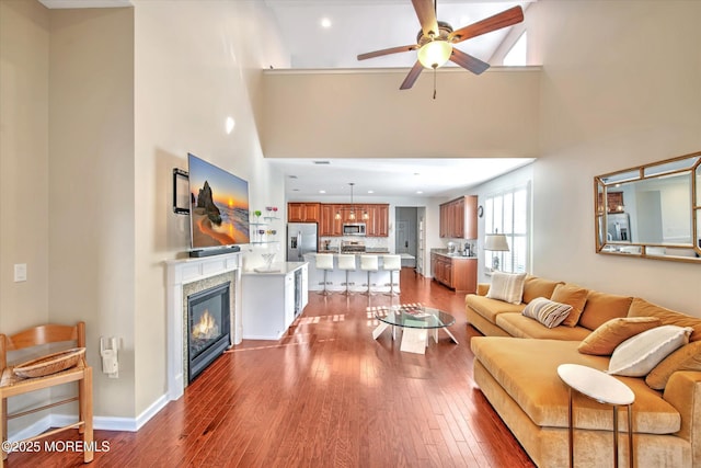 living area featuring a ceiling fan, a glass covered fireplace, baseboards, and wood finished floors