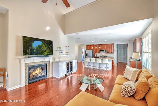 living room featuring recessed lighting, beverage cooler, wood finished floors, baseboards, and a glass covered fireplace