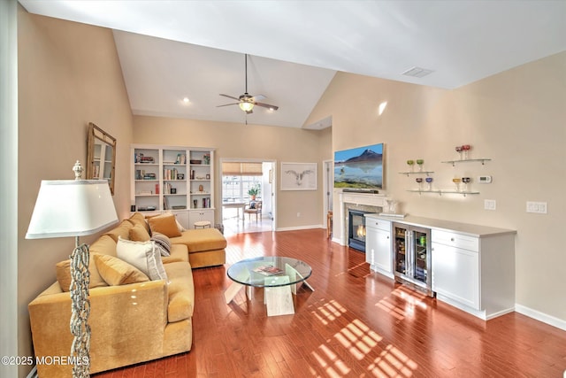 living area with hardwood / wood-style flooring, visible vents, baseboards, a ceiling fan, and a glass covered fireplace