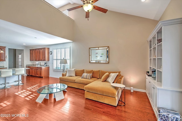 living area featuring a ceiling fan, high vaulted ceiling, baseboards, and wood finished floors