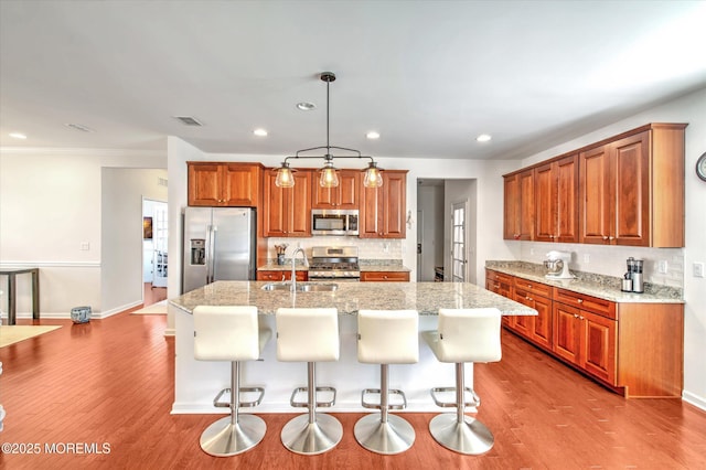 kitchen featuring pendant lighting, a breakfast bar, appliances with stainless steel finishes, brown cabinetry, and an island with sink